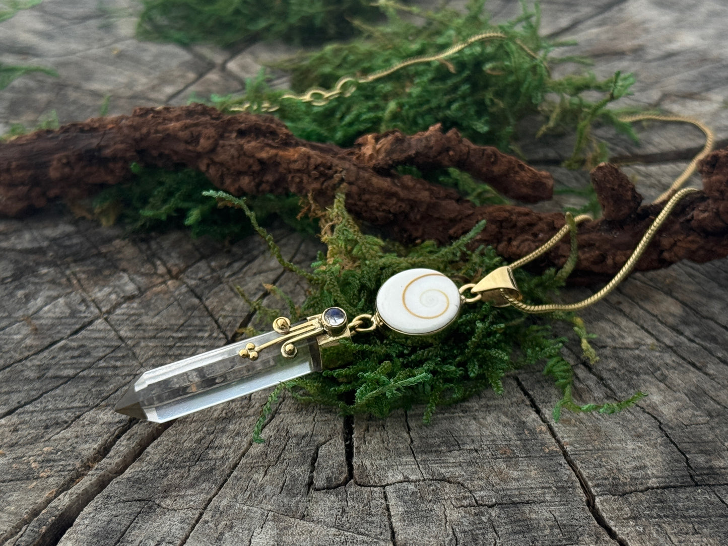 Pendant rock crystal with operculum with spirals, dots and small stone, brass