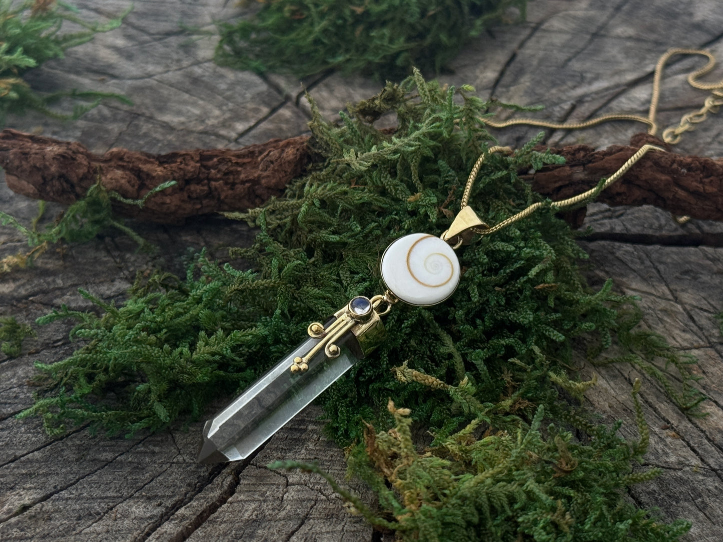 Pendant rock crystal with operculum with spirals, dots and small stone, brass 